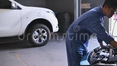 年轻的亚洲汽车机械师在汽车修理车间的汽车引擎盖检查发动机。 维修人员检查客户安全
